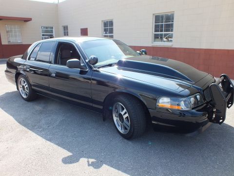 2003 Ford Crown Victoria - Side profile of a black sedan fitted with a front push bumper, parked near a warehouse