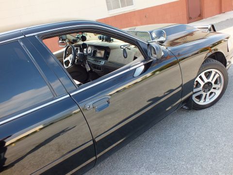 2003 Ford Crown Victoria - Door glass reveals tan cabin, center display and steering wheel; alloy wheel below