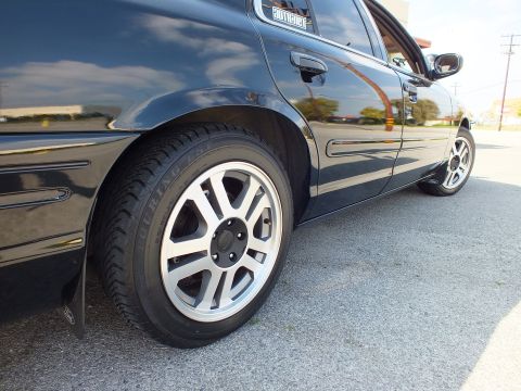 2003 Ford Crown Victoria - Close-up of a black sedan's rear quarter and machined alloy wheel with body decal above