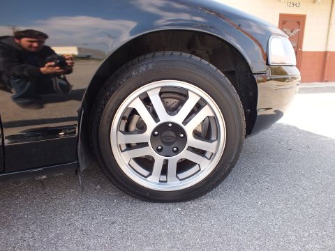 2003 Ford Crown Victoria - Detail of a black sedan's front alloy wheel; photographer reflected in the door panel