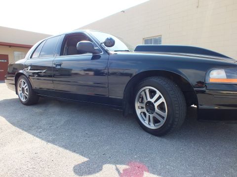 2003 Ford Crown Victoria - Low front-quarter view of a black sedan, alloy wheel and amber side marker in sunlight