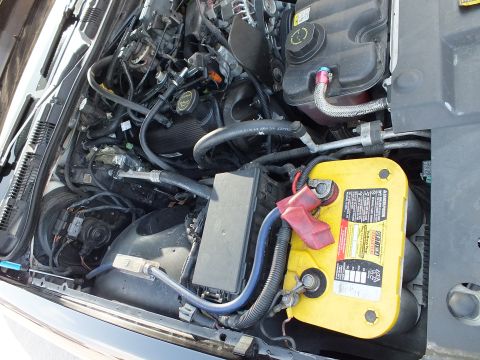 2003 Ford Crown Victoria - Left side of engine compartment showing black fuse box, harness loom and a yellow battery