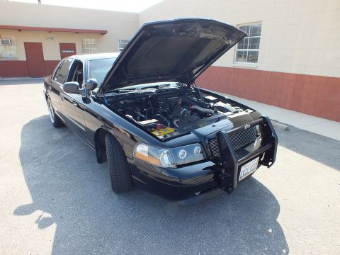 2003 Ford Crown Victoria - Black four-door sedan parked with hood raised, tubular brush guard and dark window tint