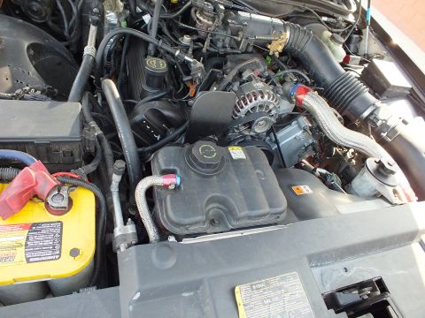 2003 Ford Crown Victoria - Engine compartment with alternator, braided hose and coolant reservoir beside a yellow battery