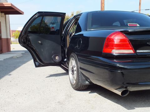 2003 Ford Crown Victoria - Rear three-quarter of a black sedan with rear door open, tinted glass and dual chrome exhaust tip