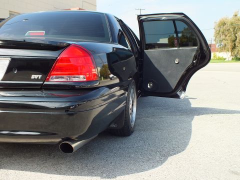 2003 Ford Crown Victoria - Rear of a black Ford sedan showing SVT badge on the trunk, red taillights and chrome exhaust tip