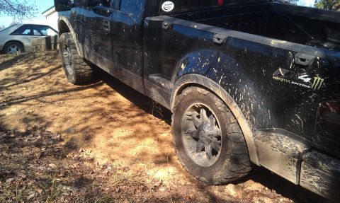 1993 Ford Bronco - A muddy black pickup truck is parked on a dirt path, with another vehicle visible in the background.