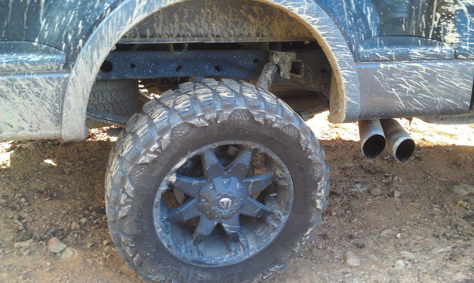 Mud-splattered truck rear wheel with aggressive tire tread and dual exhaust pipes