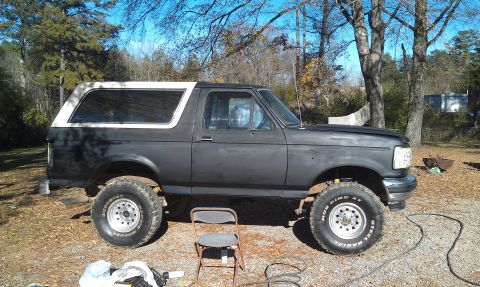 1993 Ford Bronco - A lifted 1993 Ford Bronco sits in a yard with trees in the background.