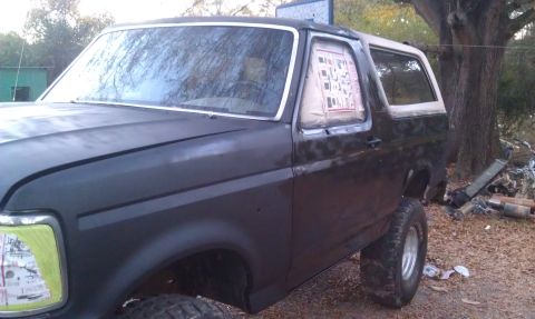 1993 Ford Bronco - This black Ford Bronco with a white top is seen from the side, appearing to be undergoing repairs or a repaint.
