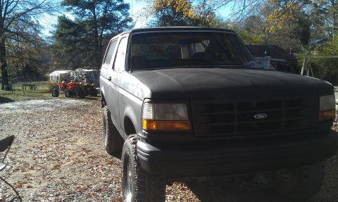 1993 Ford Bronco - The front grille and headlights of a matte black Ford Bronco are visible in this outdoor shot.