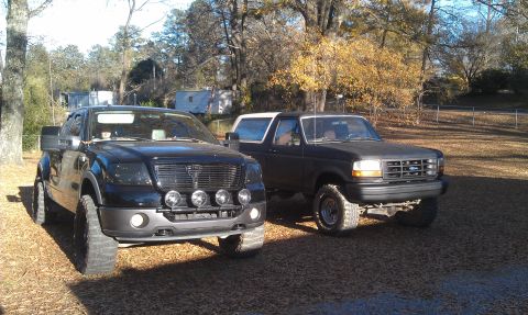 1993 Ford Bronco - Two Ford trucks, a 1993 Bronco and a later model F-150, are parked side-by-side outside.