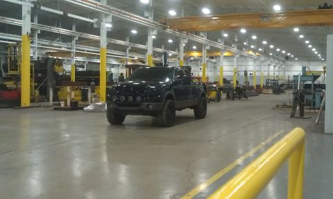 1993 Ford Bronco - A dark pickup truck sits in the middle of a factory floor with industrial equipment in the background.