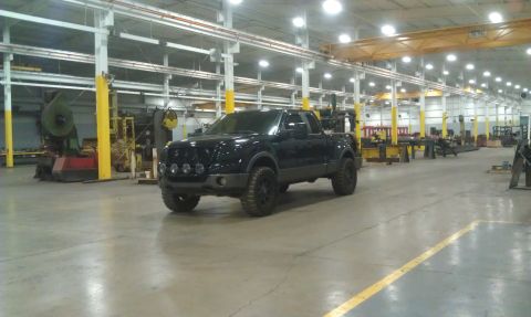 1993 Ford Bronco - A black pickup truck is parked inside a large industrial building with machinery in the background.