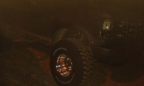 1993 Ford Bronco - Close-up of a 1993 Ford Bronco's front grille and tire at night.