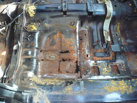 1975 Ford Ranchero - The interior floor of a vehicle shows extensive rust damage and missing metal sections.