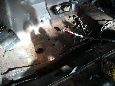 1975 Ford Ranchero - The interior floor pan shows significant rust and damage, with a wiring harness and loose bolts visible.