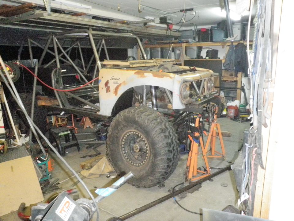 Custom off-road vehicle in garage, front end visible, large tires, roll cage, rusty body panels