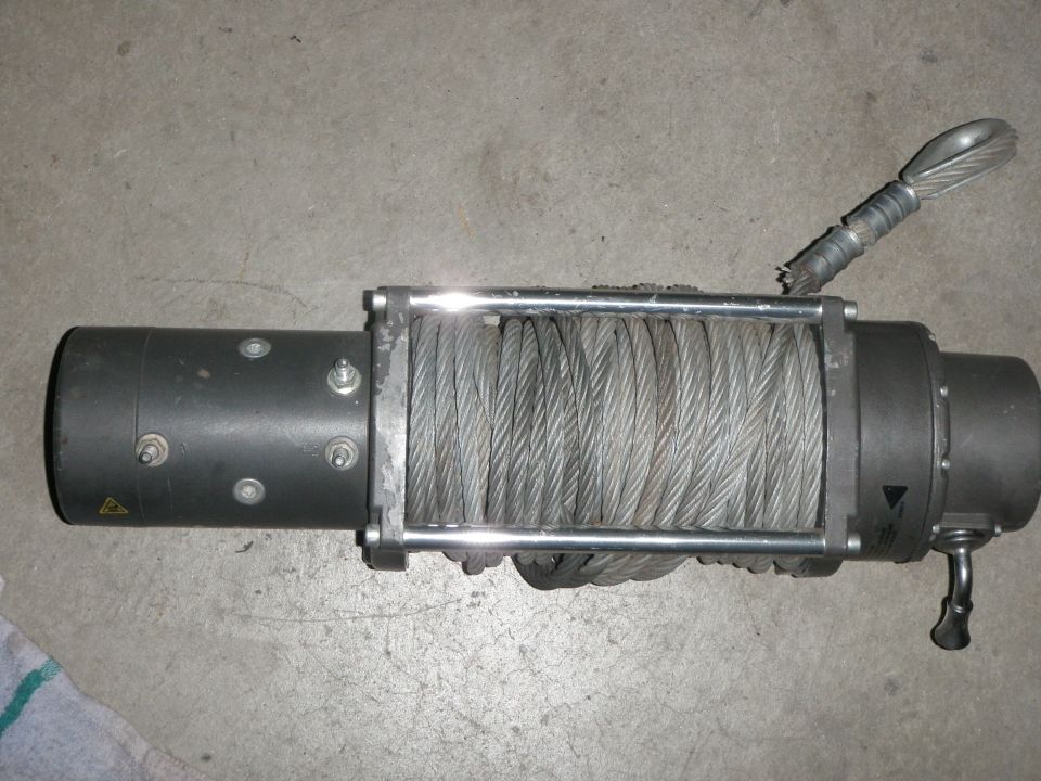 Gray winch with coiled steel cable and a metal hook attached to a frayed cable end