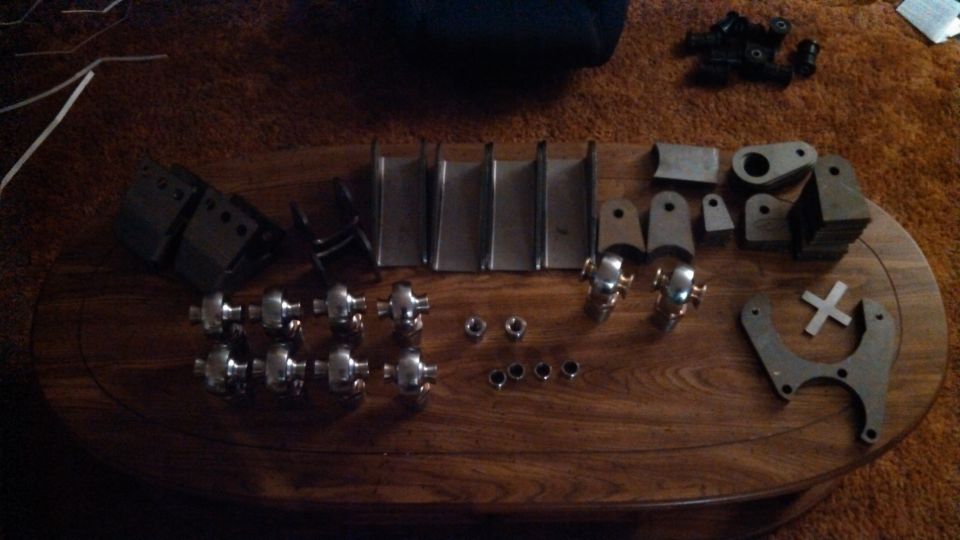 Assortment of metal brackets, u-joints, nuts, and washers laid out on a wooden table