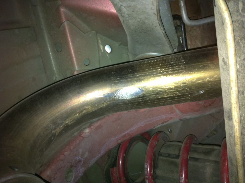Close-up of a curved exhaust pipe over red coil springs and undercarriage components