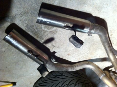 1995 Ford Mustang - Close-up of two shiny exhaust pipes, likely aftermarket, with rubber hangers attached.