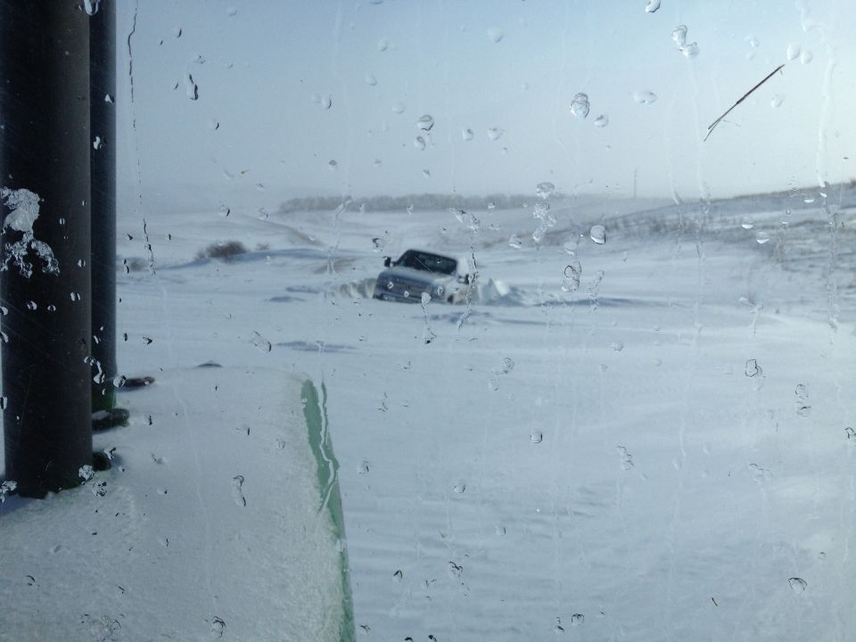 White SUV stuck in deep snow, viewed through a rain-streaked window