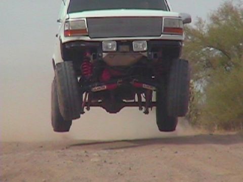 1992 Ford Bronco - This lifted truck is airborne, its suspension and tires against a dusty background.