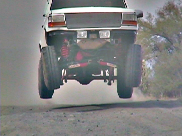 White SUV jumping on dirt trail, rear underside and exhaust visible mid-air