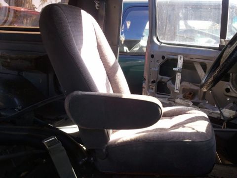 1994 Ford Bronco - The interior of a vehicle shows a worn passenger seat and an open door, with another vehicle partially visible in the background.