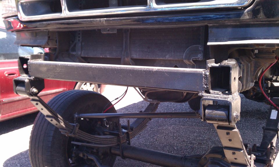 Custom front bumper and suspension parts on a vehicle, with a red vehicle in the background