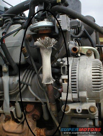1994 Ford Bronco - Close-up view of an engine component a braided metal sleeve over a pipe, likely part of the exhaust system.