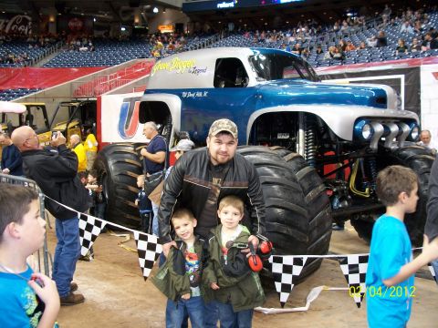 1989 Ford Bronco - A family poses for a photo in front of a monster truck at an indoor event.