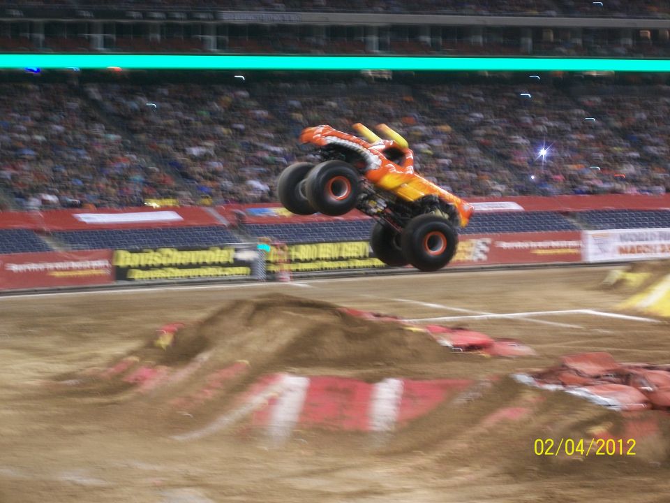 Monster truck mid-air over a dirt ramp, with stadium seating in the background