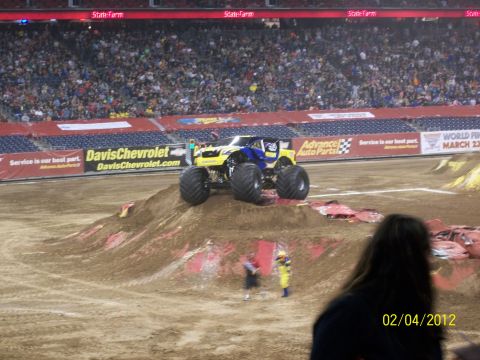 1989 Ford Bronco - A monster truck sits atop a dirt ramp in a stadium, ready for action.