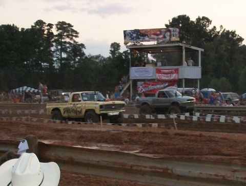 1989 Ford Bronco - Trucks compete in a mud bogging event with a grandstand and trees visible.