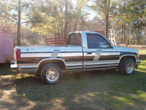 1989 Ford Bronco - A side view of a pickup truck parked outdoors on a grassy area with trees in the background.