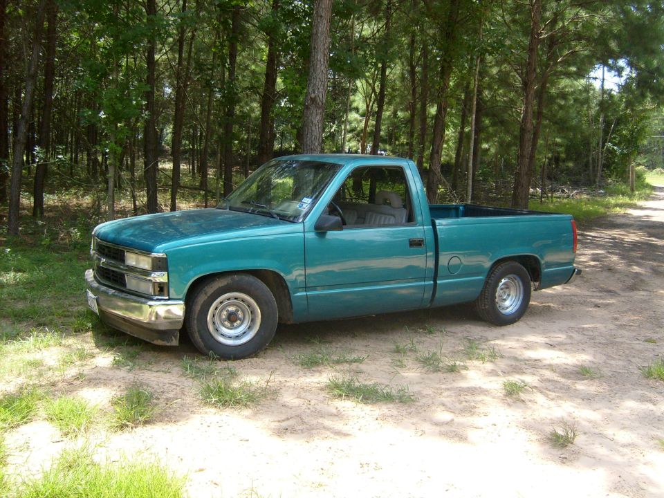 Teal 1995 Chevrolet C/K pickup truck parked on a dirt road with trees in the background