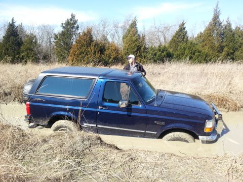 1995 Ford Bronco - A 1995 Ford Bronco is stuck in a muddy ditch with dry grass and trees in the background.