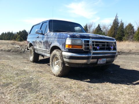 1995 Ford Bronco - Mud-covered 1995 Ford Bronco sits on a dirt path under a clear blue sky.