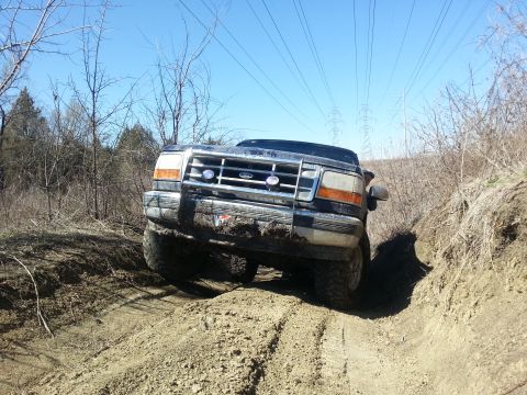 1995 Ford Bronco - This Ford Bronco is navigating a challenging off-road trail with steep inclines and muddy terrain.
