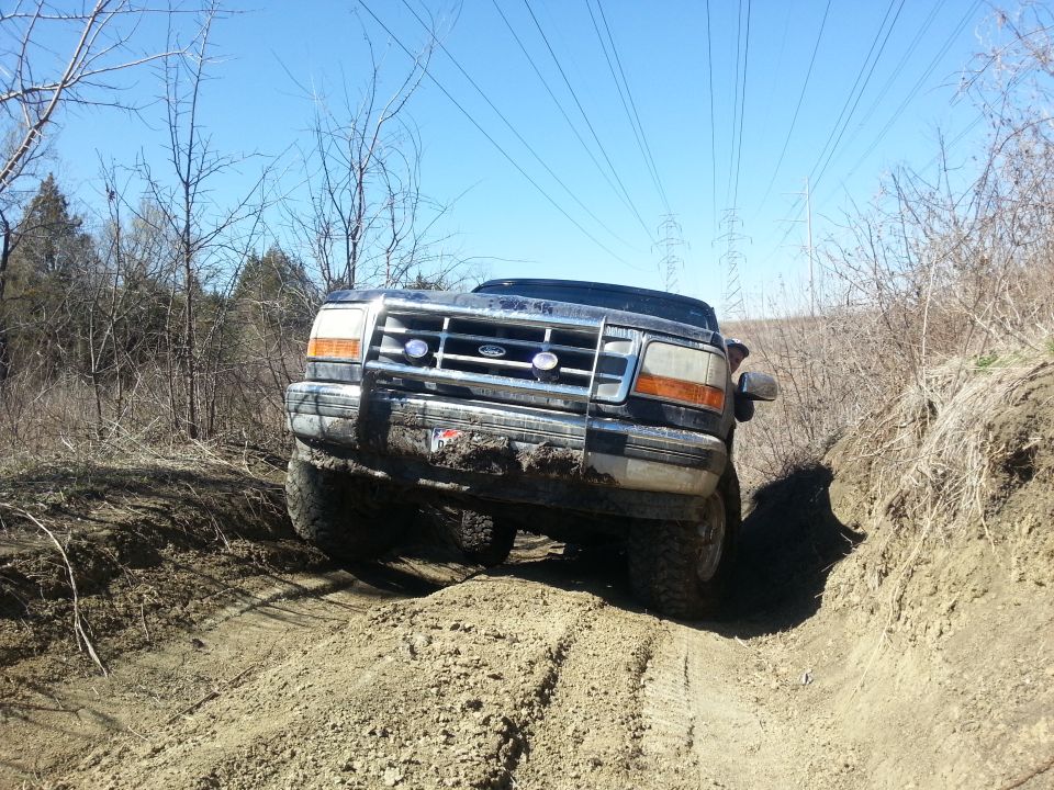 Black Ford Bronco on a dirt trail, front view, mud on grille and bumper