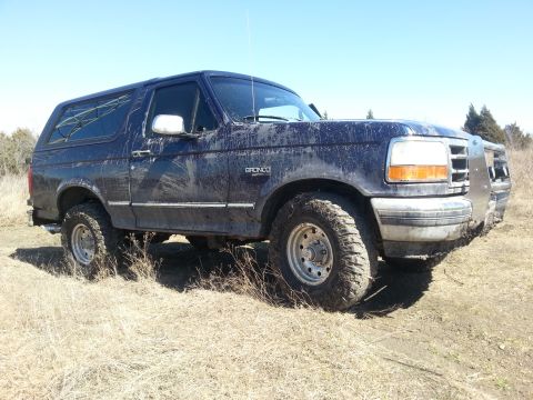 1995 Ford Bronco - Mud-covered 1995 Ford Bronco sits in a field under a clear blue sky.