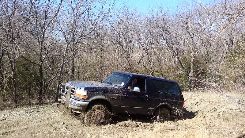 Dark blue Ford Bronco stuck in mud on a wooded trail