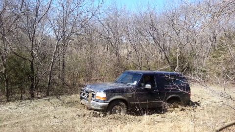 1995 Ford Bronco - Ford Bronco navigating a muddy off-road trail surrounded by bare trees.