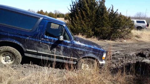 1995 Ford Bronco - A blue 1995 Ford Bronco is stuck in the mud, with another SUV in the background.