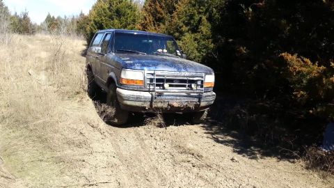 1995 Ford Bronco - A blue Ford Bronco navigates a muddy trail, its front end angled towards the viewer.