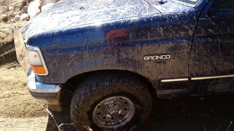 1995 Ford Bronco - This 1995 Ford Bronco is heavily covered in mud, showing its front quarter panel and wheel.