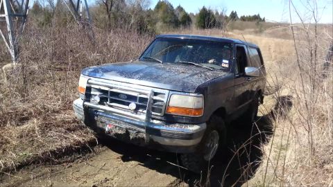 1995 Ford Bronco - Ford Bronco navigating a muddy off-road path with dry vegetation surrounding it.