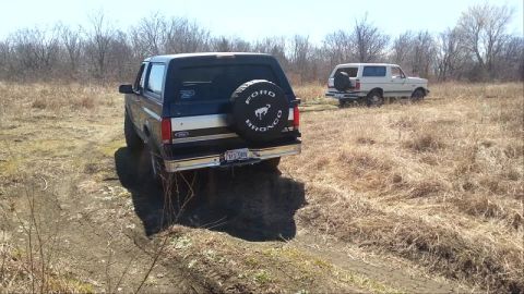 1995 Ford Bronco - Two Ford Broncos are seen off-roading in a dry, grassy field under a clear sky.